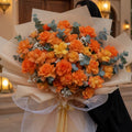 Bouquet of orange and yellow flowers held by a person in front of a building entrance.