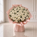 A large bouquet of white roses wrapped in light pink paper, displayed on a reflective light beige floor against an elegant white paneled wall.