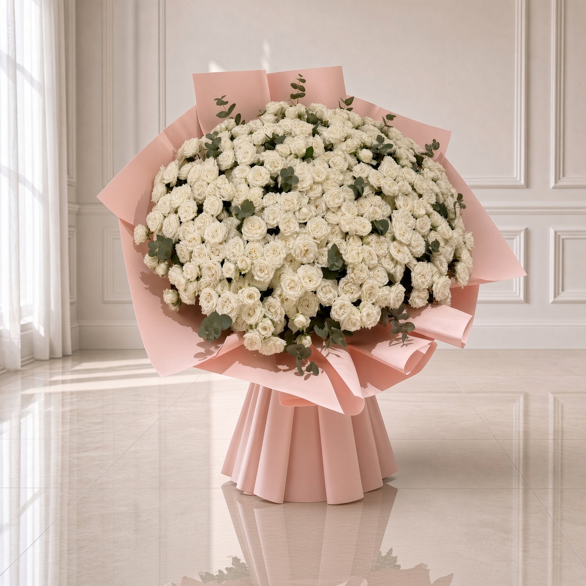 A large bouquet of white roses wrapped in light pink paper, displayed on a reflective light beige floor against an elegant white paneled wall.