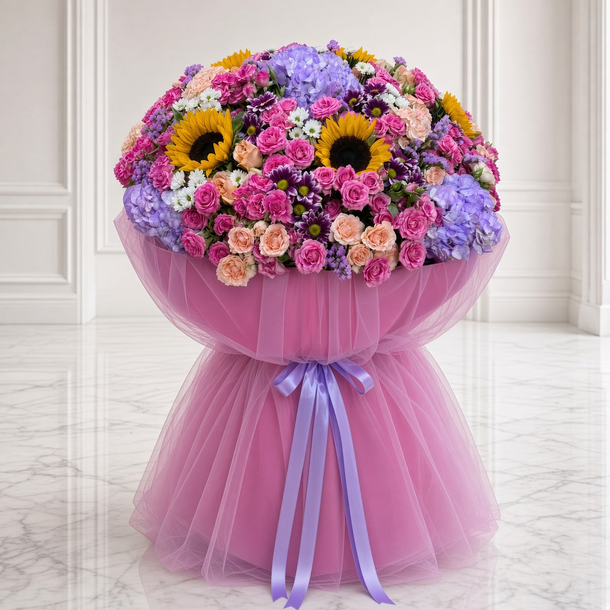 A large, vibrant floral bouquet wrapped in pink tulle and tied with a purple ribbon, displayed on a light marble floor against a white paneled wall.